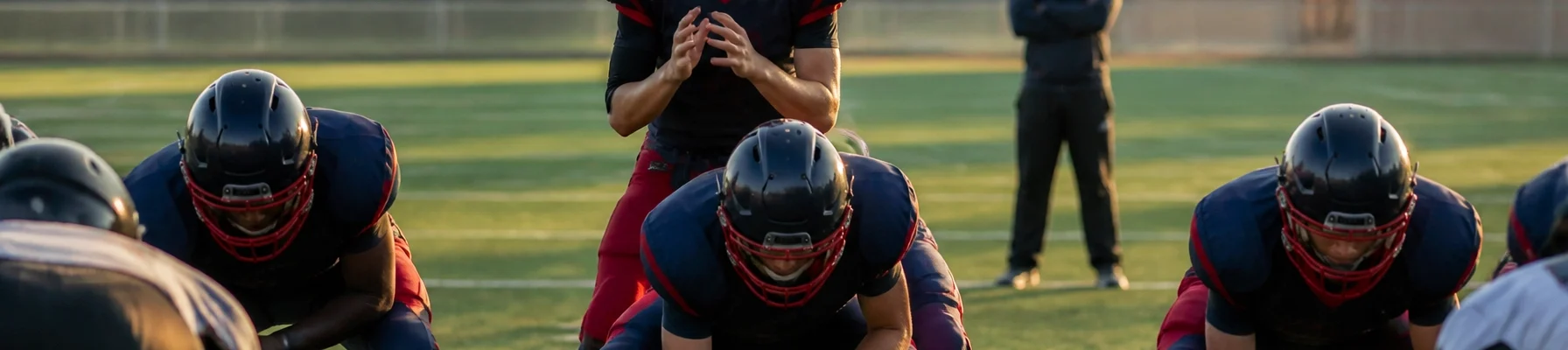 Quarterback behind the offensive line, holding the ball at the line of scrimmage during a football drill on a sunlit field.